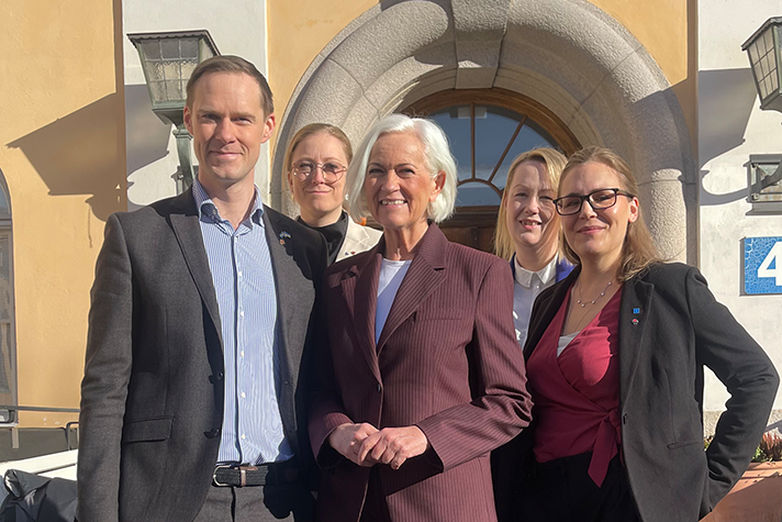 Fem personer framför en äldre gul byggnad.