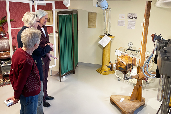 Tre kvinnor tittar på äldre sjukvårdsutrustning.