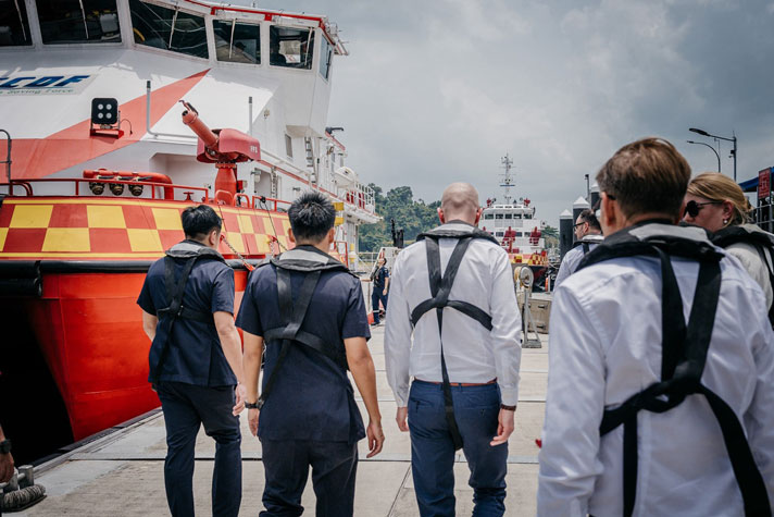 Carl-Oskar bakifrån med singaporianer och ett rödgult fartyg.