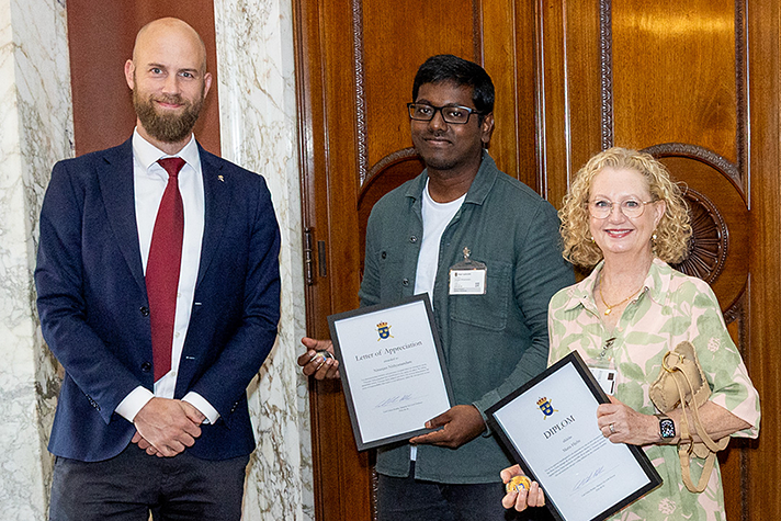 Ministern med Maria Hjelte och Niranjan Nithyanandam, som håller diplom i händerna.