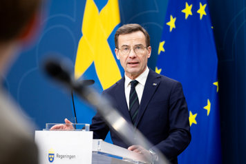 Kristersson fotograferad i halvfigur mot en fond av svenska flaggan och EU-flaggan