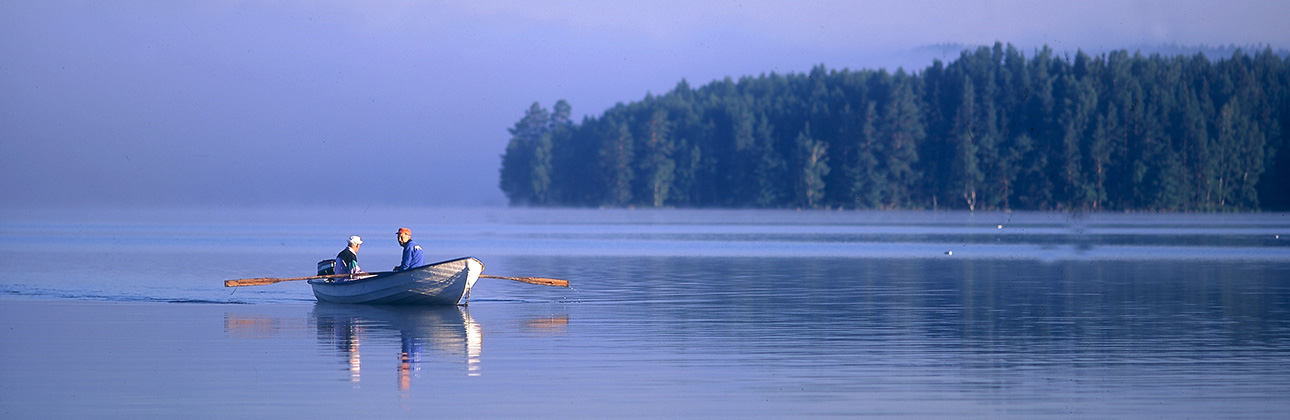 Två män sitter i en roddbåt på en insjö en tidig morgon.