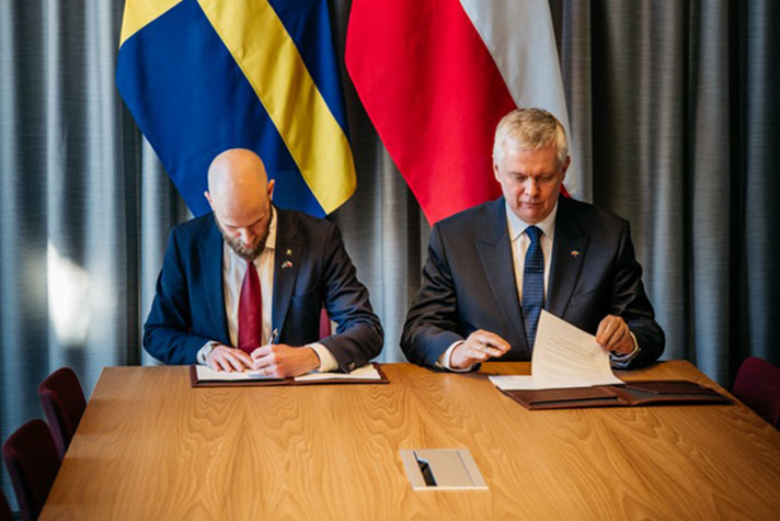 Två personer sitter bredvid varandra och skriver under ett papper. 