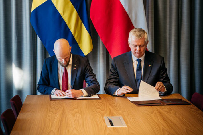 Två personer sitter bredvid varandra och skriver under ett papper.