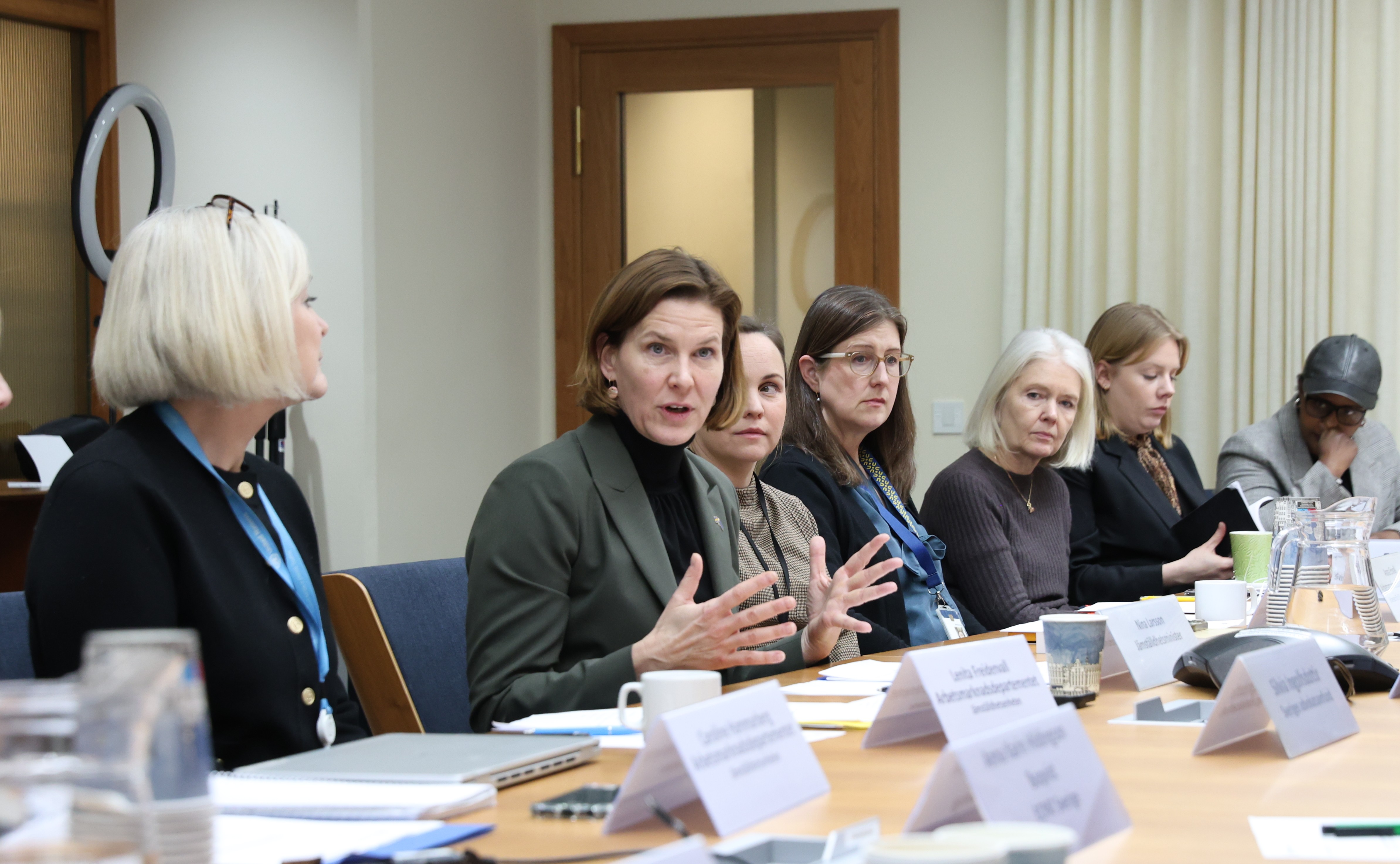 Jämställdhetsminister Nina Larsson har samlat till en möte runt ett bord.