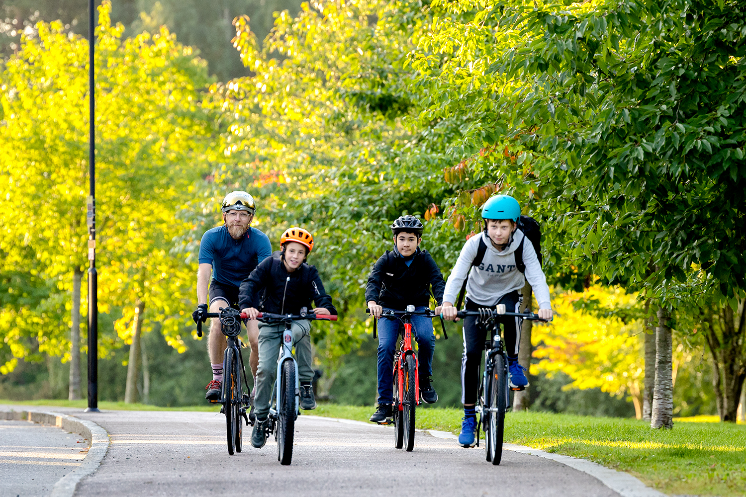 En man och tre barn cyklar i det gröna.