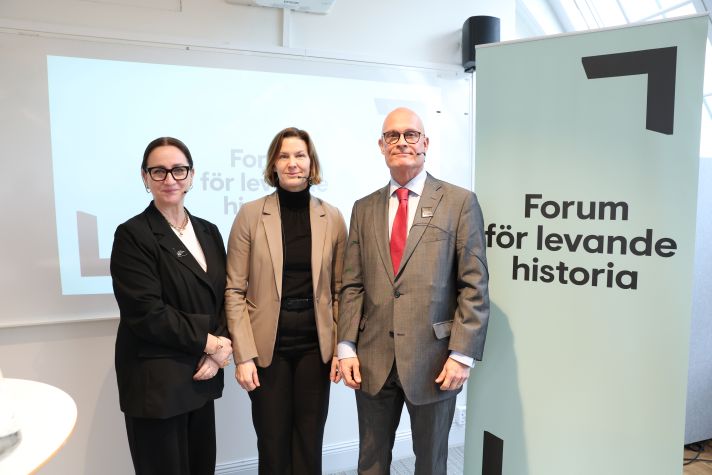 Petra Mårselius, Nina Larsson och Oscar Österberg står sidan om varandra. Till höger syns en roll-up med texten Forum för levande historia och i bakgrunden syns en whiteboard.