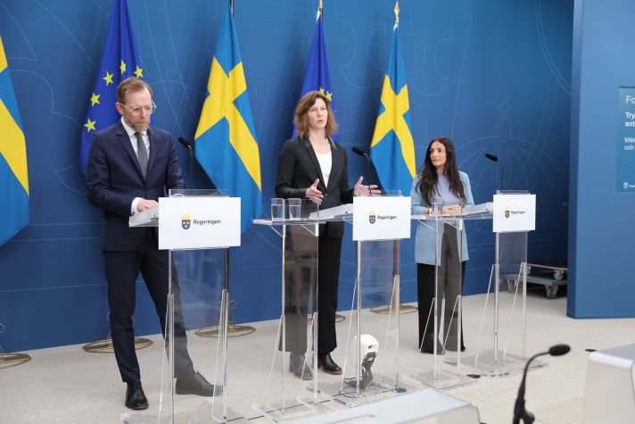 Tre statsråd står vid sina talarstolar och pratar inför en publik