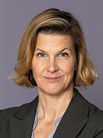 Jämställdhetsminister Nina Larsson står framför en grå vägg och tittar in i kameran.