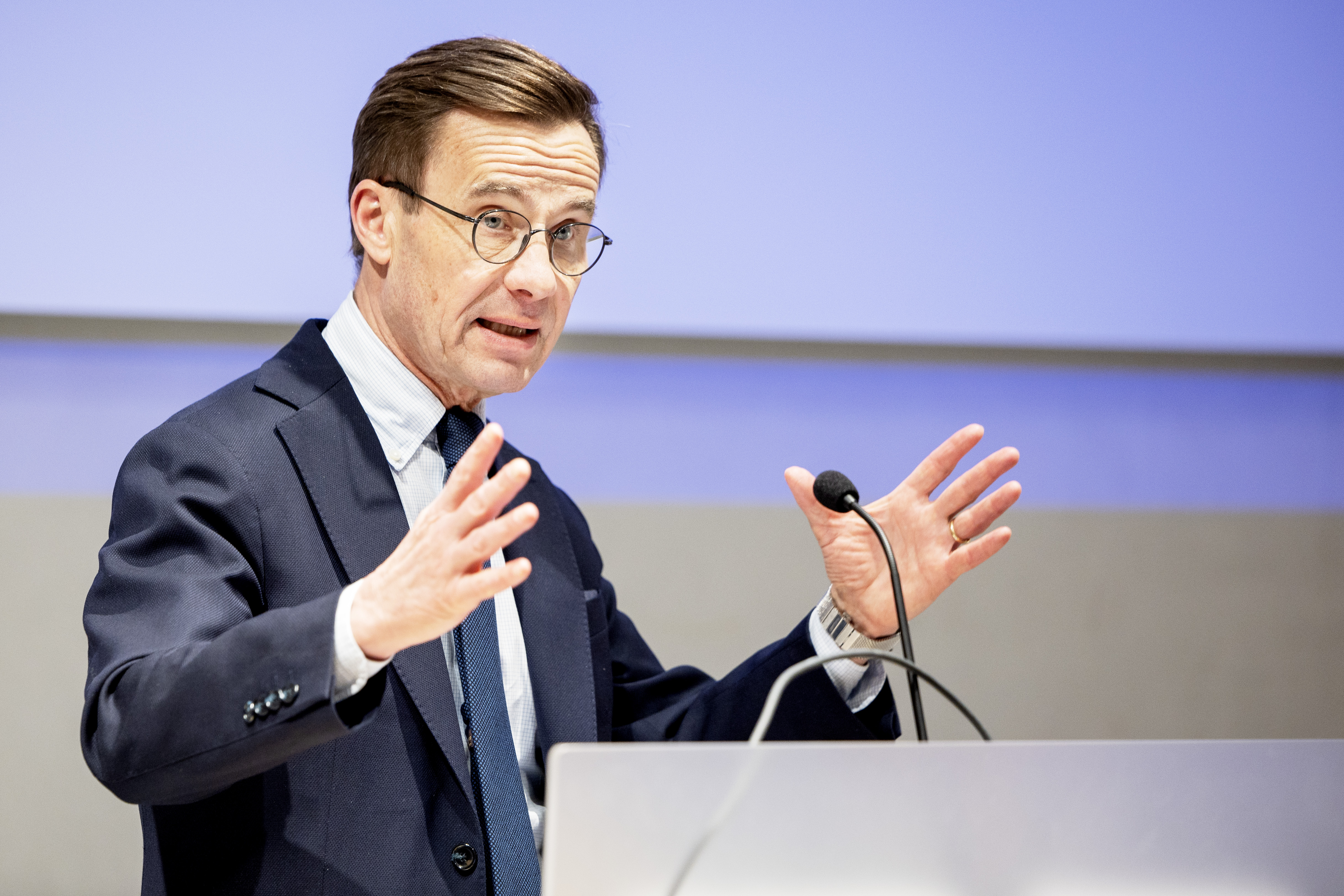 Statsminister Ulf Kristersson står bakom ett vitt talarpodium och håller tal.