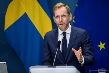 Jakob Forssmed talar på presskonferensen. Bakom honom en blå bakgrund med svenska flaggan och EU-flaggan.