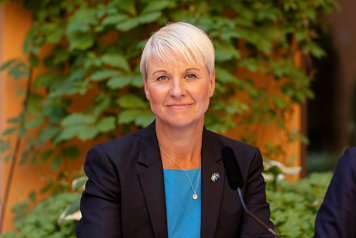 Äldre- och socialförsäkringsminister Anna Tenje utomhus i svart kavaj, ler mot kameran.