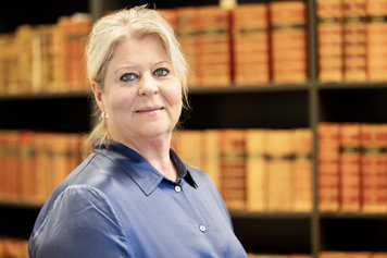 Socialtjänstminister Camilla Waltersson Grönvall står framför bokhylla vänd mot kameran iklädd blå blus.