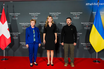 Schweiz president Viola Amherd, Sveriges vice statsminister Ebba Busch och Ukrainas president Volodymyr Zelenskyj står bredvid varandra. Till höger står den ukrainska flagga och till vänster den schweiziska. På väggen bakom står det skrivet Summit on Peace in Ukraine. 