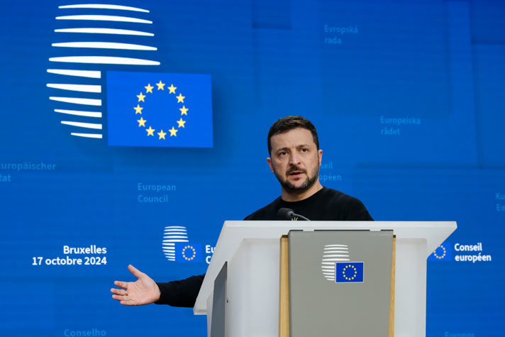 Ukrainas president Zelenskyj står bakom en talarstol. I bakgrunden syns Europeiska rådets logotype mot en blå bakgrund och EU-flaggan.