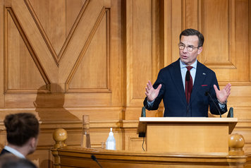 Ulf Kristersson står i en talarstol i förstakammarsalen i riksdagen.