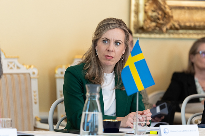 Jessica Rosencrantz sitter vid ett bord i ett konferensrum. På bordet står en svenska flagga.