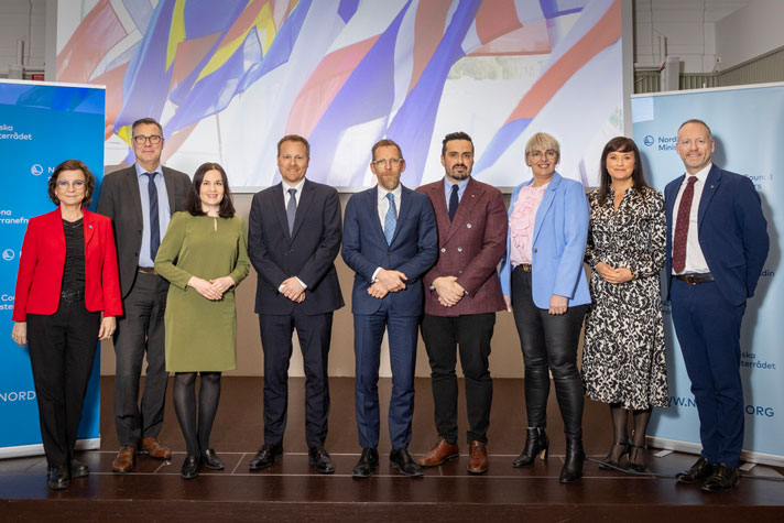 Socialminister Jakob Forssmed (i mitten) står tillsammans med ministerkollegor från Finland, Danmark, Norge, Island, Färöarna och Åland i ett rum. I bakgrunden syns skärmar med bilder på flaggor.