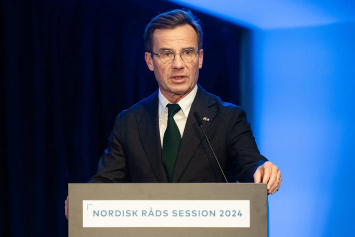 Statsministern står i en talarstol med texten Nordisk råds session 2024. I bakgrunden syns en blå vägg.