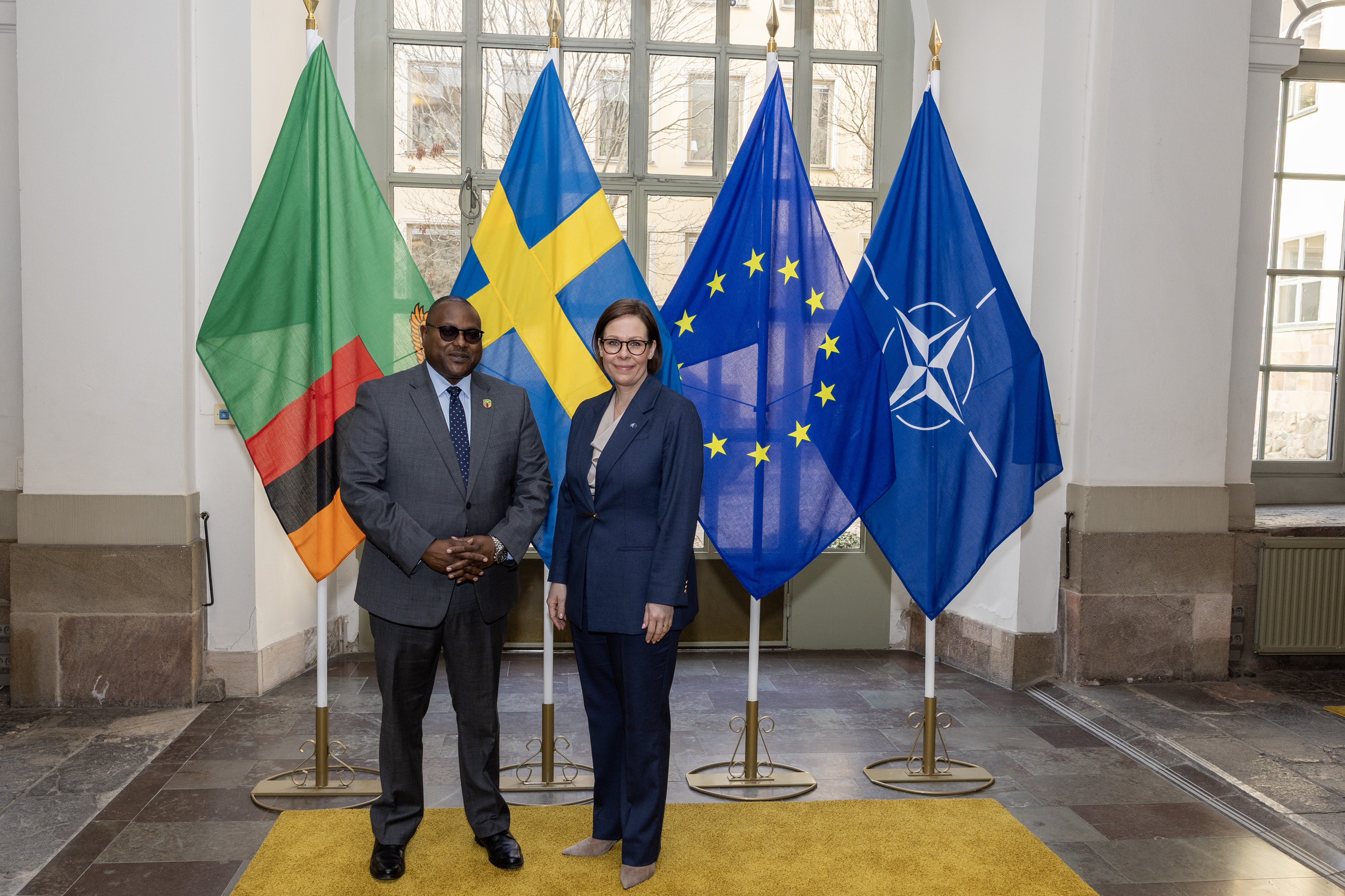 Maria Malmer Stenergard och Mulambo Haimbe står framför svensk flagga och zambisk flagga.