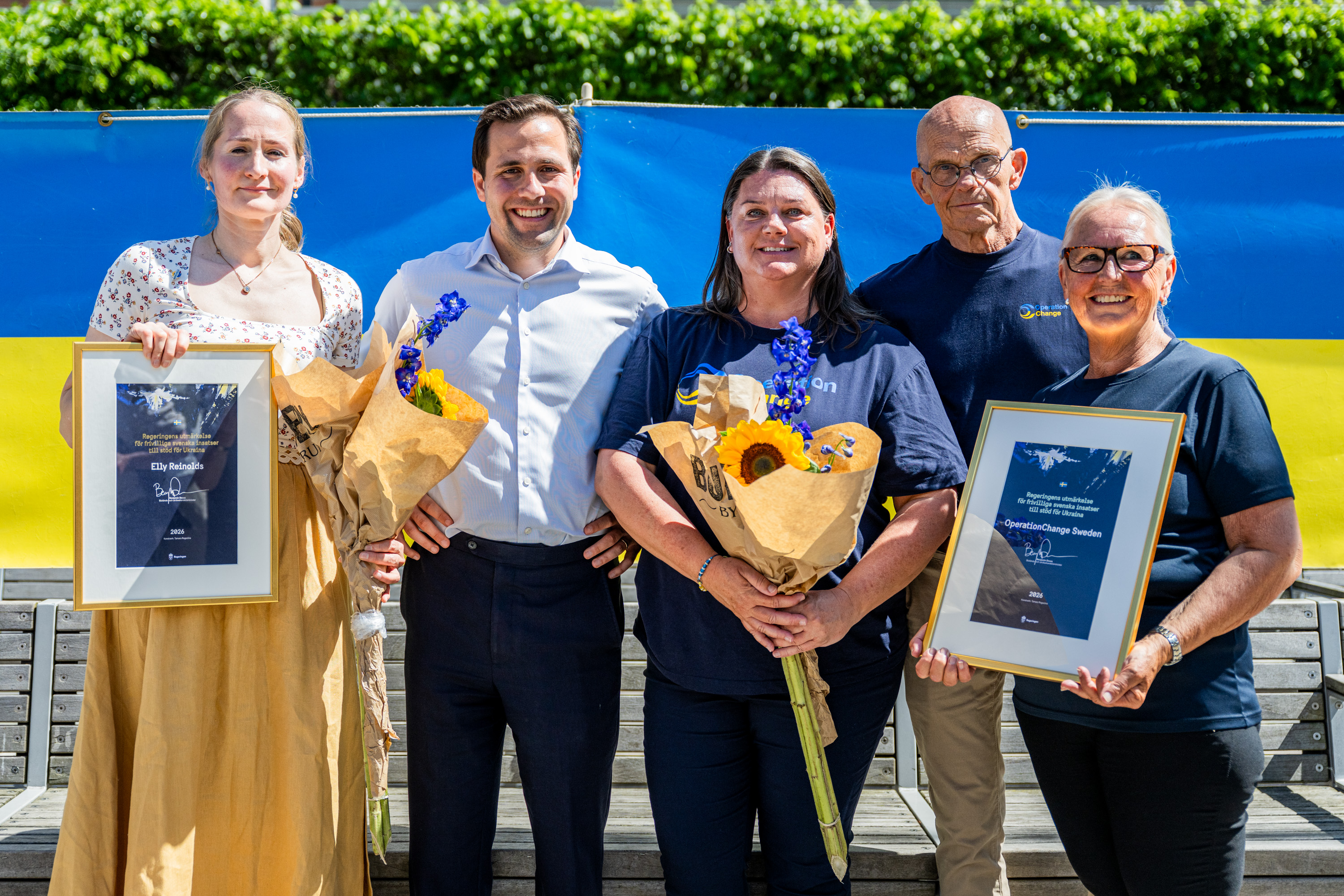 Benjamin Dousa tillsammans med Elly Reinolds och medarbetare från OperationChange. Mottagarna håller i diplom och blommor.