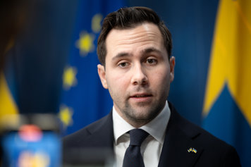 Benjamin Dousa på pressträff framför svensk flagga och EU flagga.